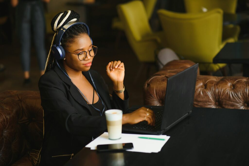 Happy black girl in wireless headphones studying online, using laptop and taking notes